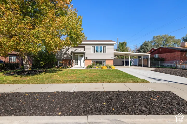 Split-level exterior featuring a brick and horizontal siding facade, covered carport, concrete driveway, and front lawn