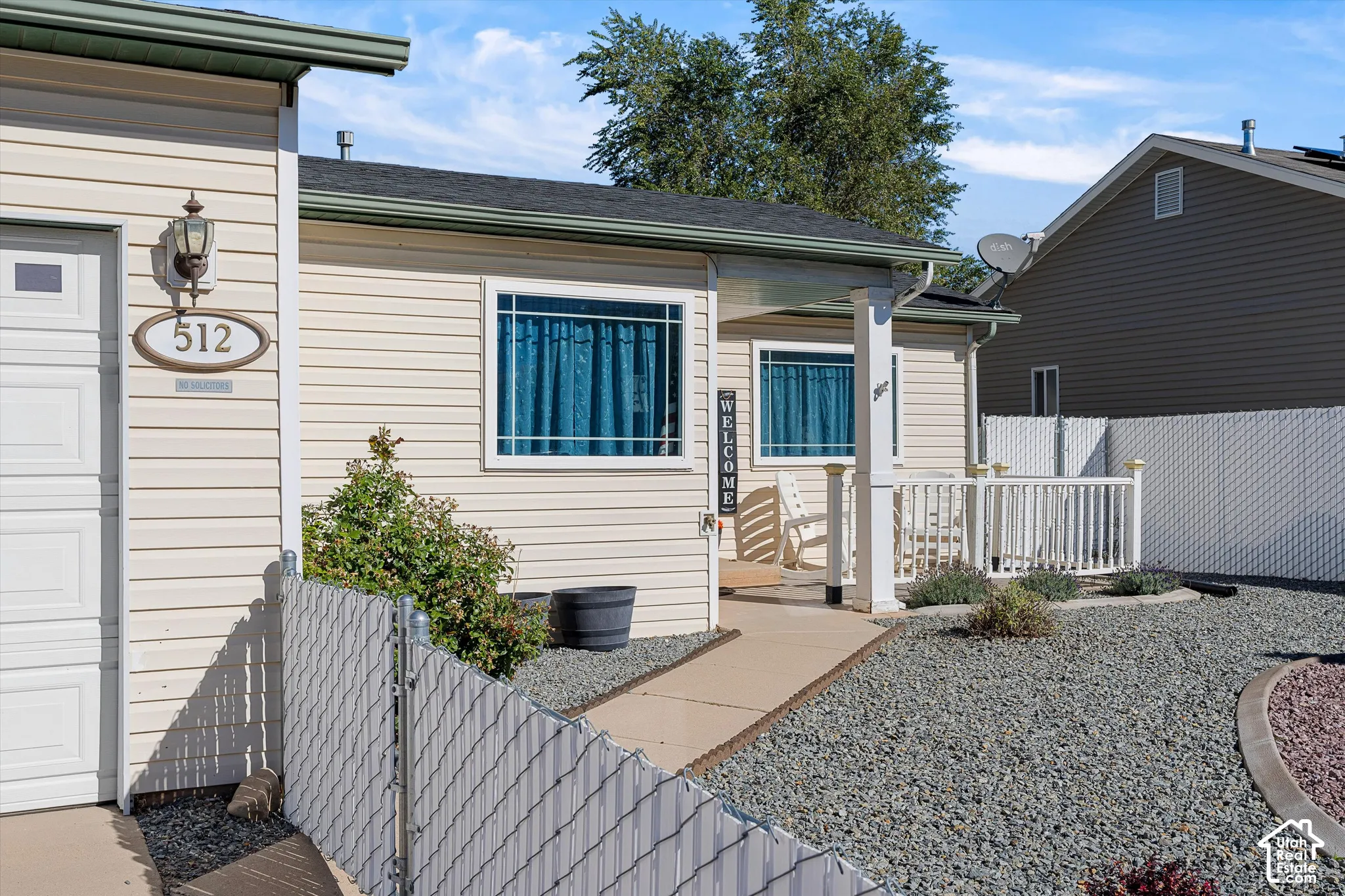 Light-colored horizontal siding exterior featuring a covered front porch with a white balustrade, an integrated garage, and a low-maintenance gravel landscape