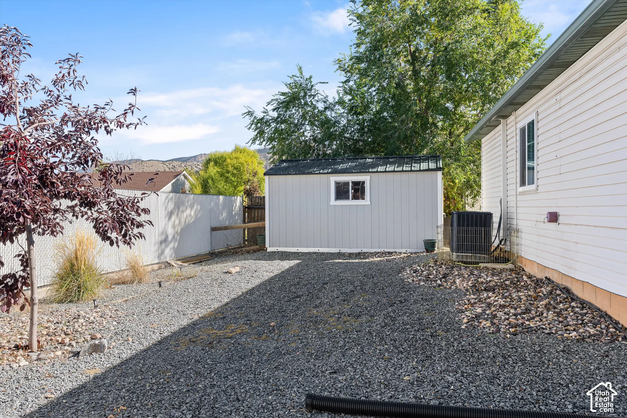 Side yard featuring gravel ground cover, a detached storage structure with a single-pane window, horizontal siding, and solid vinyl fencing
