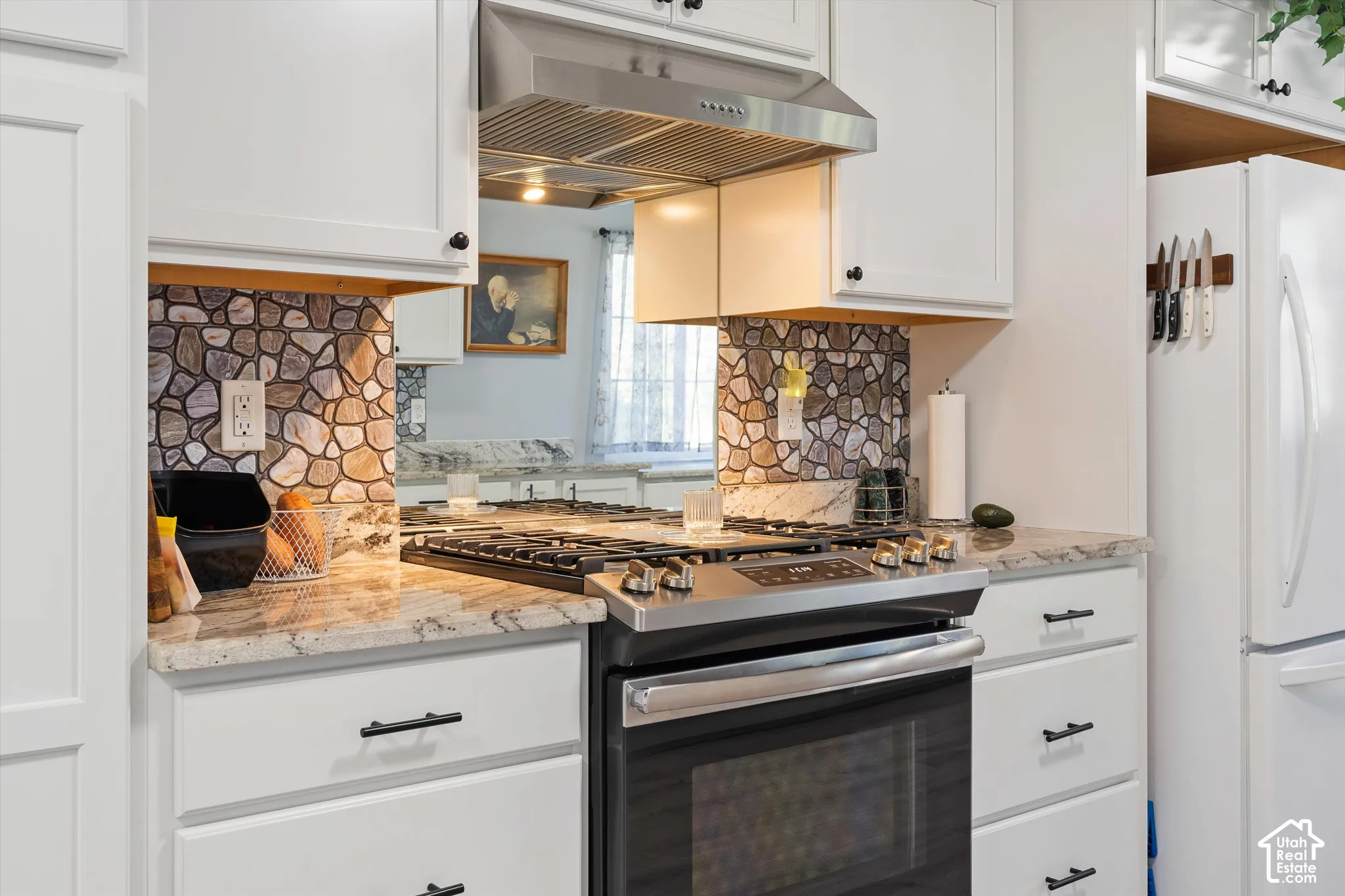 Kitchen featuring white shaker-style cabinetry, stone-surface countertops, decorative stone-patterned backsplash, stainless steel range, and stainless steel range hood