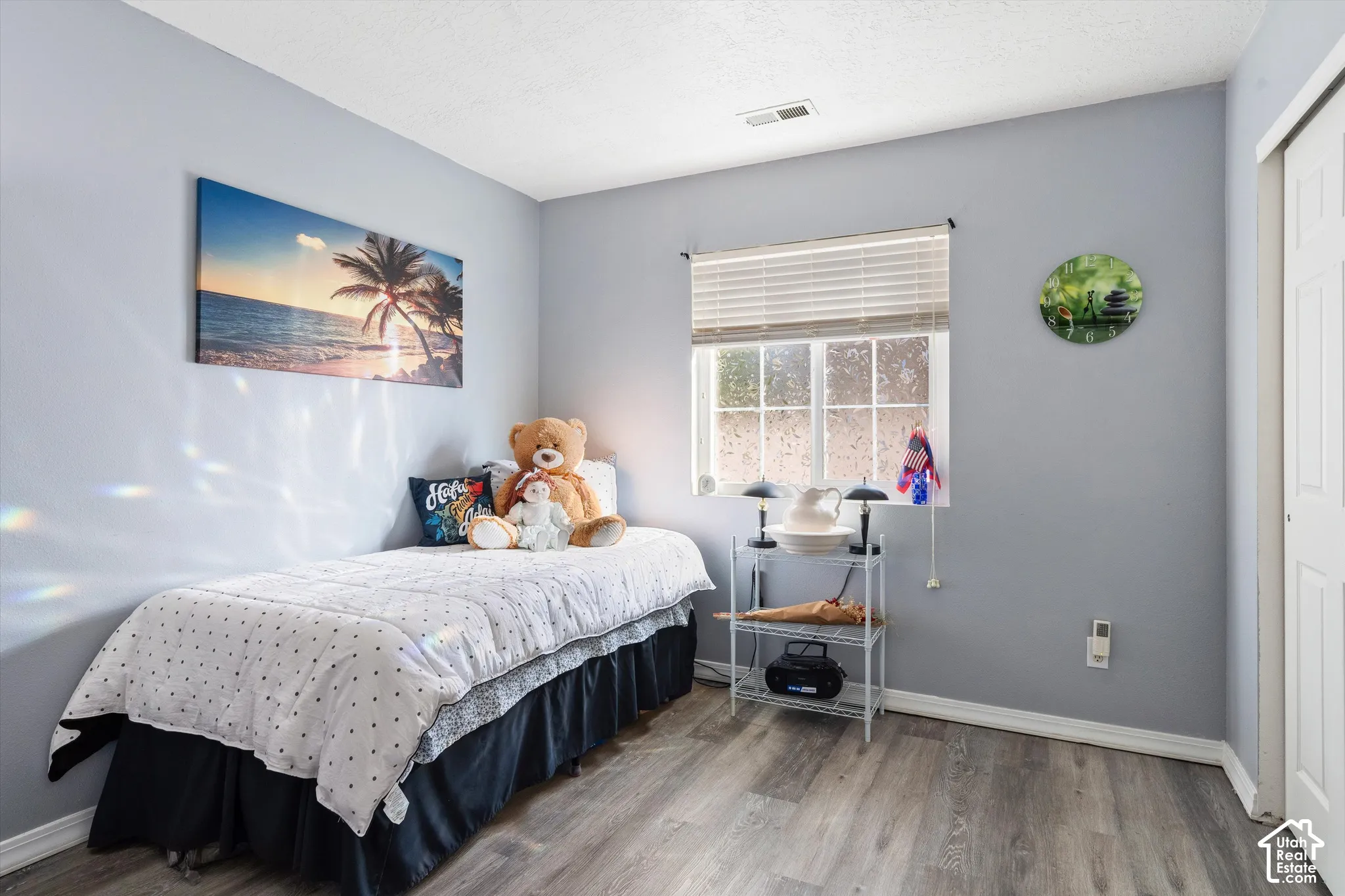 Room featuring wood-finish flooring, neutral wall paint, a multi-pane window with horizontal blinds, and a white paneled sliding closet door