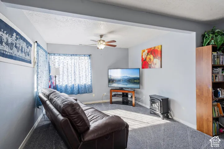 Living area featuring wall-to-wall carpeting, ceiling fan with integrated lighting, and a freestanding hearth stove