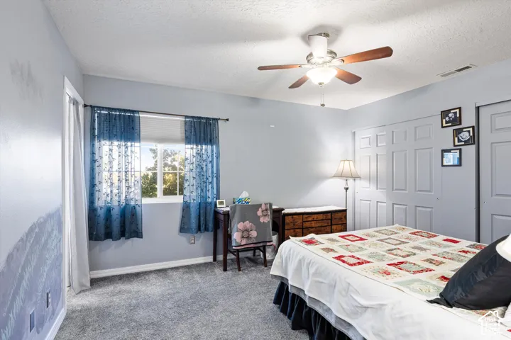 Neutral-toned bedroom featuring carpeting, multi-panel sliding closet doors, and a ceiling fan with integrated lighting
