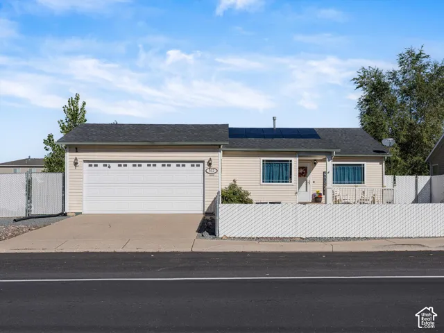 Single-level residence featuring horizontal siding, an attached two-car garage, roof-mounted solar panels, and perimeter chain-link fencing