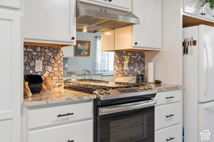 Kitchen featuring white shaker-style cabinetry, stone-surface countertops, decorative stone-patterned backsplash, stainless steel range, and stainless steel range hood