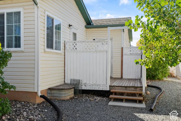 Exterior elevation featuring light-colored horizontal siding, wood decking with white lattice privacy screening, and a corrugated metal window well cover