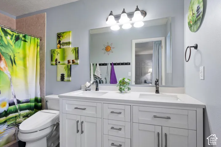 Dual-sink vanity with white cabinetry, solid-surface countertop, dark hardware, and a large plate-glass mirror featuring a four-light fixture