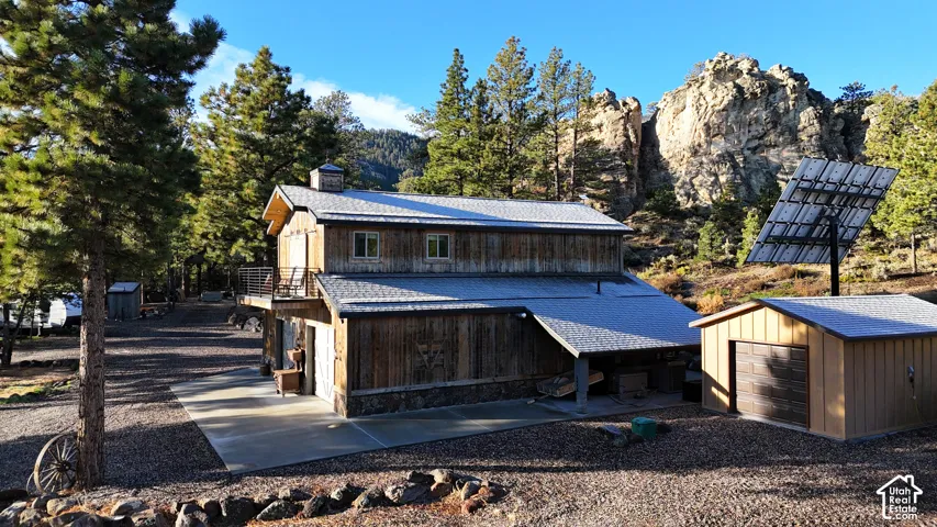 Rustic wood-sided structure featuring an elevated deck, metal roofing, ground-level concrete patio, detached garage, and solar panel array