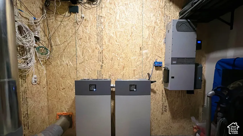 Utility area featuring dual energy storage units, wall-mounted inverter system, and oriented strand board wall paneling