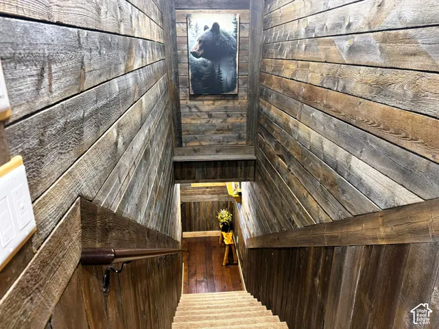 Staircase featuring horizontal reclaimed wood-plank wall paneling, stained wood handrail, and wood-finish flooring at the landing