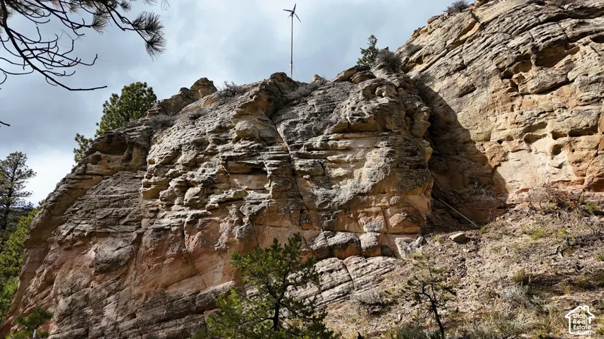Natural rock formation featuring exposed sandstone strata, native evergreen trees, and an installed wind turbine