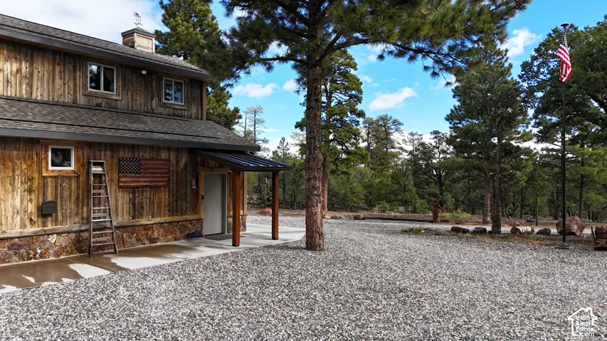 Rustic exterior featuring vertical wood siding, stone veneer base, covered entryway with dark metal roofing, and gravel grounds situated among mature pine trees