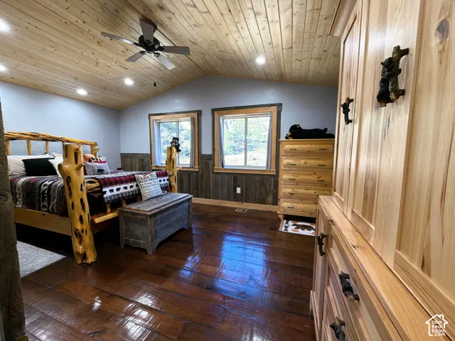 Vaulted wood-plank ceiling featuring recessed lighting and a ceiling fan, dark-toned wood-finish flooring, two-tone wall treatment with lower-level dark wood paneling, and dual windows with natural wood casing