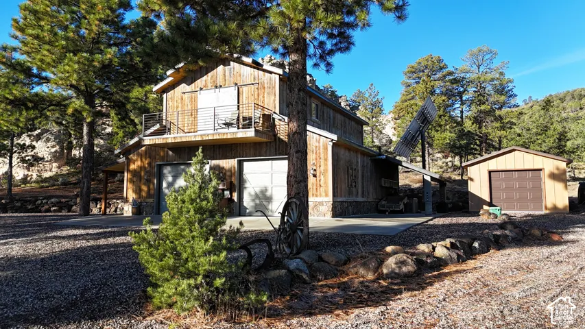 Multi-level structure featuring vertical wood siding, stone veneer foundation, metal balcony railing, dual garage bays, and solar panel array