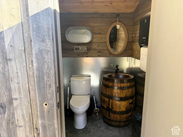 Restroom featuring rustic wood-plank walls, a stainless steel backsplash, a vanity base constructed from an upcycled barrel, and an integrated basin sink