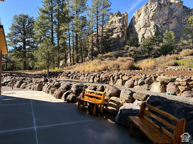 Concrete patio featuring a natural stone retaining wall, mature pine trees, and mountainous rock formations