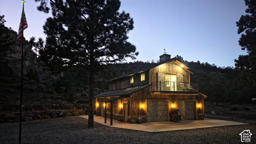 Rustic two-story structure featuring a wood-plank exterior, metal roof, stone foundation, attached upper-level balcony with metal railing, and dual-bay garage doors