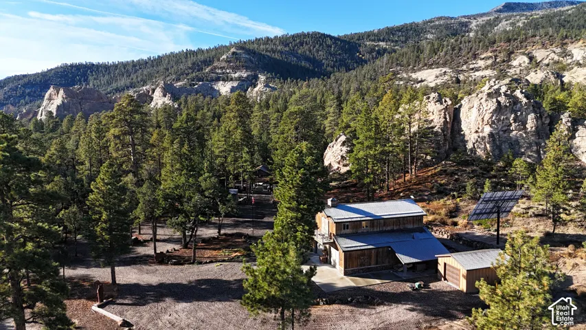 Multi-level wood-clad exterior featuring a metal roof, detached garage, ground-mounted solar array, and expansive forested acreage with rock outcroppings