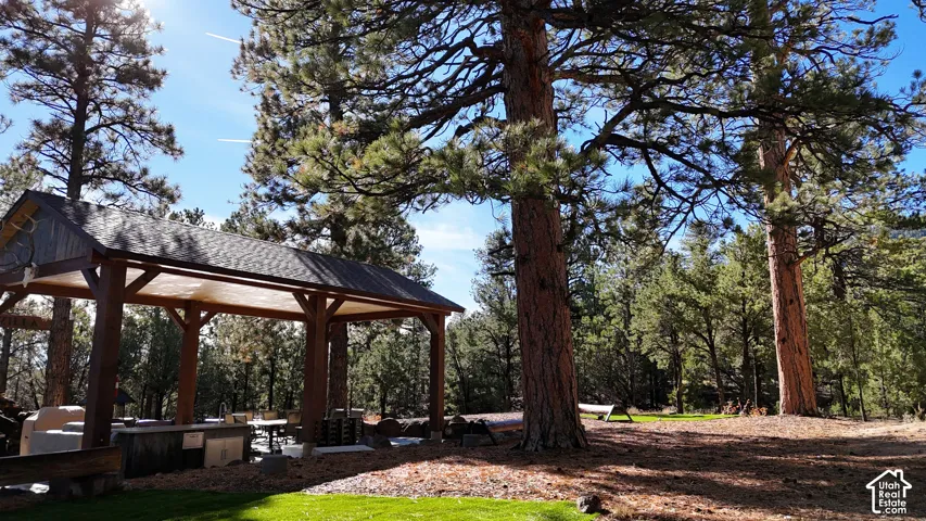 Outdoor pavilion featuring exposed timber framing, shingle roofing, and a built-in outdoor kitchen, set within a landscape of mature pine trees