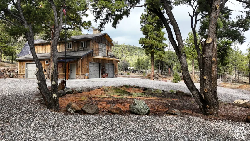 Two-story exterior featuring vertical wood siding, stone base masonry, metal roofing, dual garage bays, and a second-level balcony with metal railing