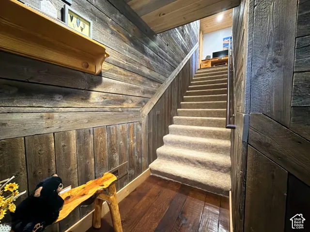Staircase featuring reclaimed wood wall paneling, wide-plank wood flooring, carpeted treads, and a built-in wooden ledge