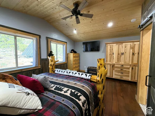 Vaulted wood-plank ceiling featuring a mounted ceiling fan and recessed lighting, custom built-in wood cabinetry, and dark-toned wood-finish flooring