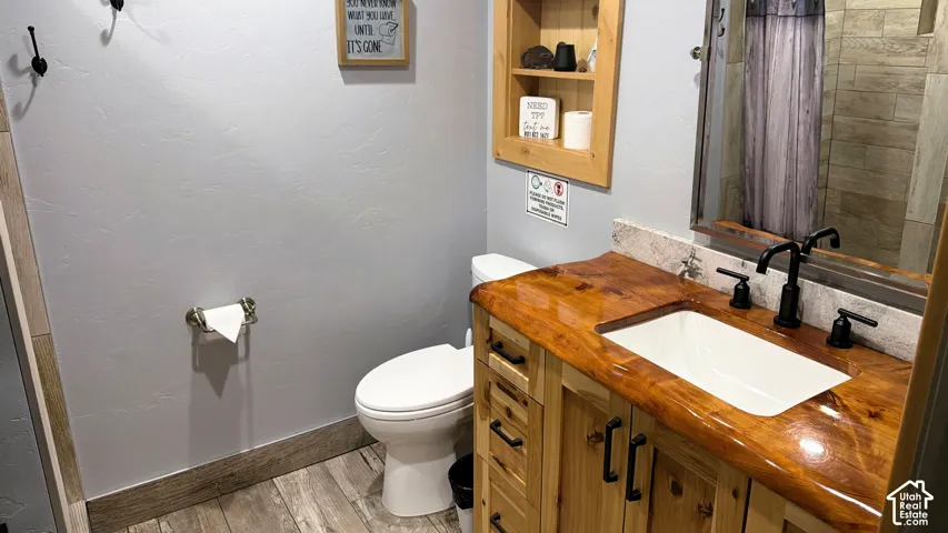Custom wood vanity with a natural-edge countertop, drop-in sink, matte black widespread faucet, recessed wall shelving, and wood-finish flooring