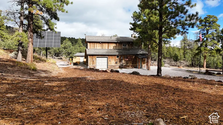 Two-story wood siding exterior featuring a stone foundation, asphalt shingle roof, attached garage, and ground-mounted solar panel array