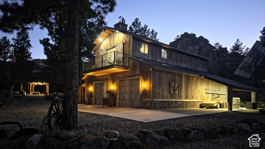 Rustic timber-clad structure featuring a stone masonry foundation, second-story balcony with metal railing, two sliding-style garage bays, and a covered lean-to area