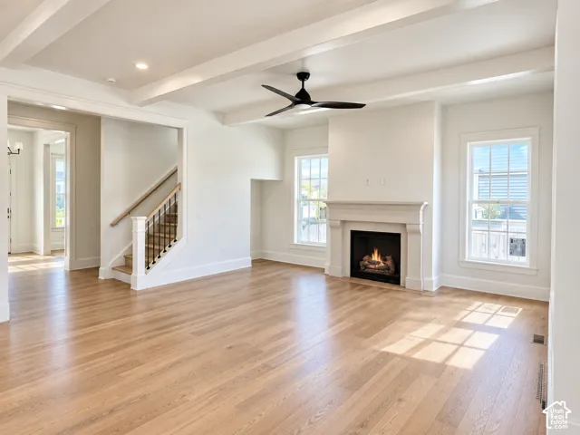 Living area featuring wood-finish flooring, ceiling beams, a matte black ceiling fan, and a fireplace with a decorative mantel
