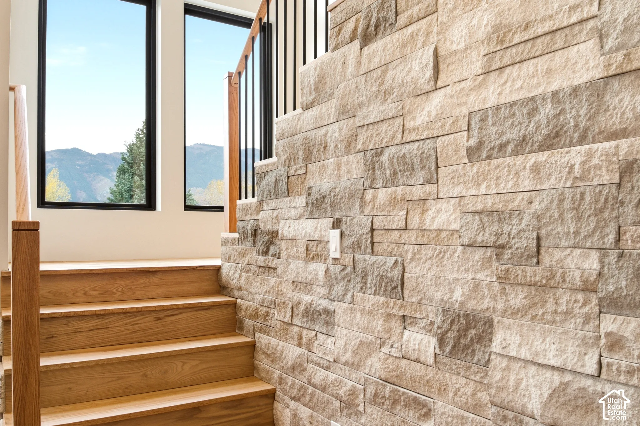 Natural limestone accent wall paired with a staircase railing composed of oak handrails and black metal vertical balusters