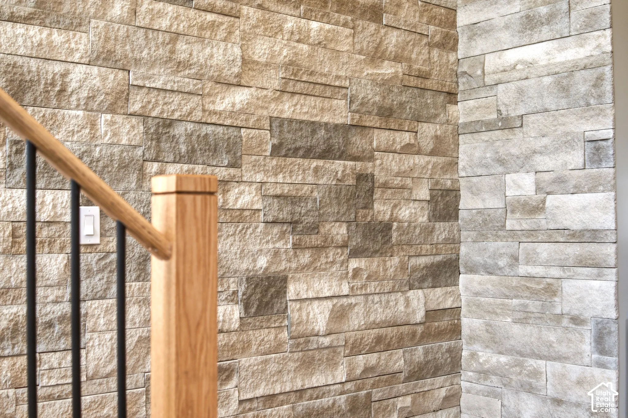 Natural limestone accent wall paired with a staircase railing composed of oak handrails and black metal vertical balusters