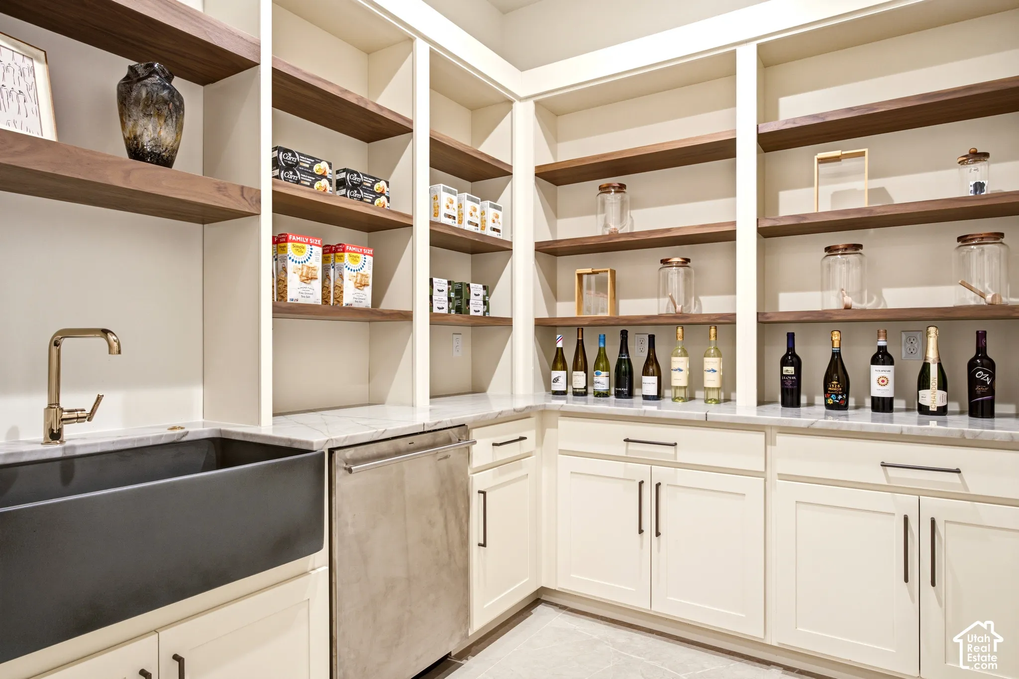 Walk-in butlers pantry featuring custom walnut shelving, Ivory Taj Quartz countertops, ash grey farmhouse-style sink, Kohler French Gold faucet, and stainless steel monogram dishwasher