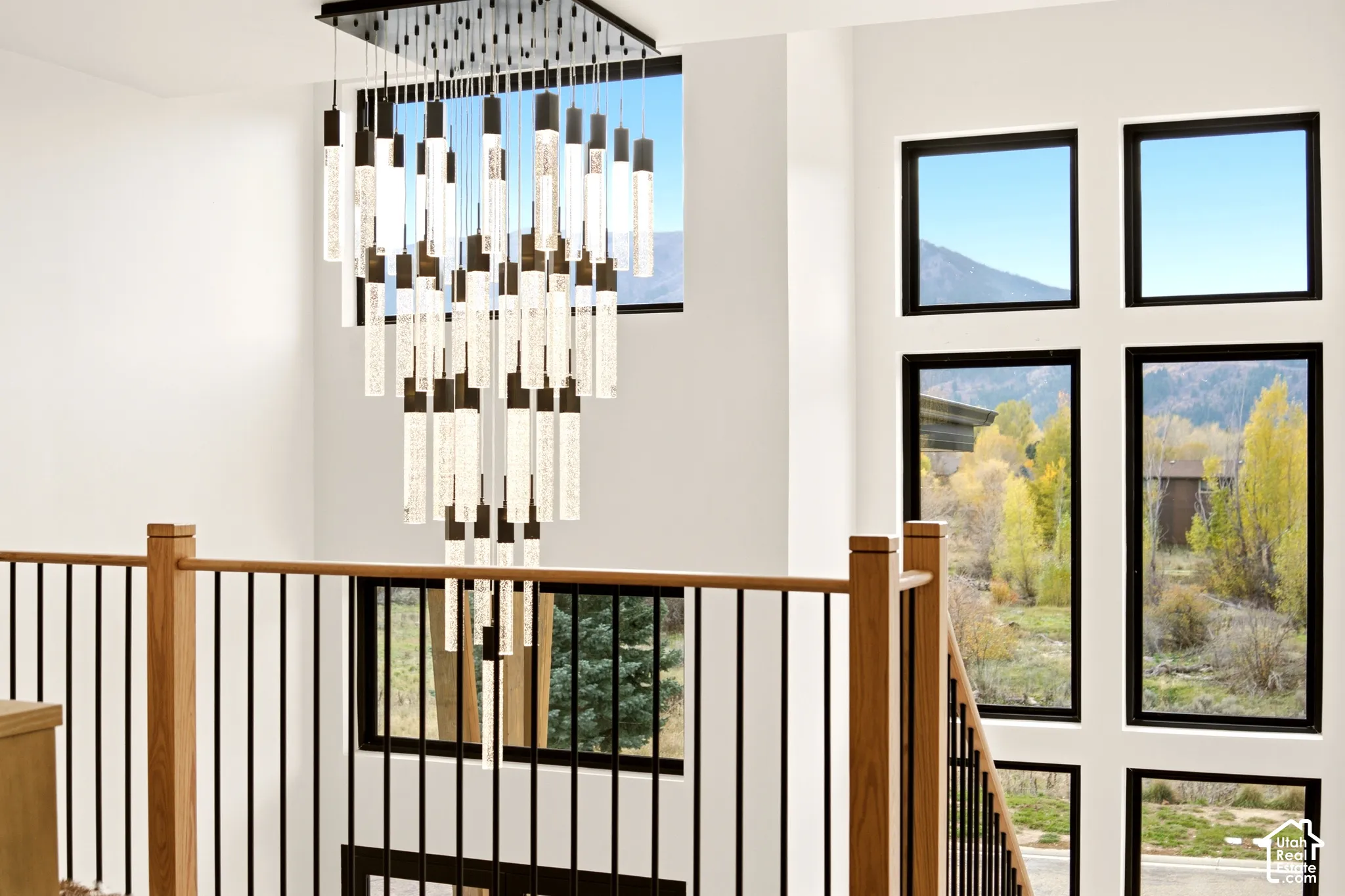 Multi-tiered statement chandelier, floor-to-ceiling windows, and a oak-topped railing with vertical metal balusters