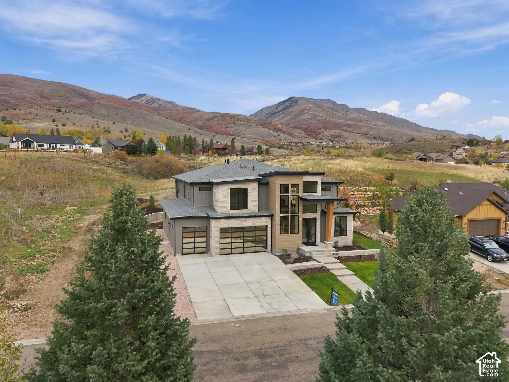 Contemporary exterior featuring dry-stacked natural limestone facade, multi-story glass paneling, double full view glass-paneled garage doors, set against a prominent mountain backdrop