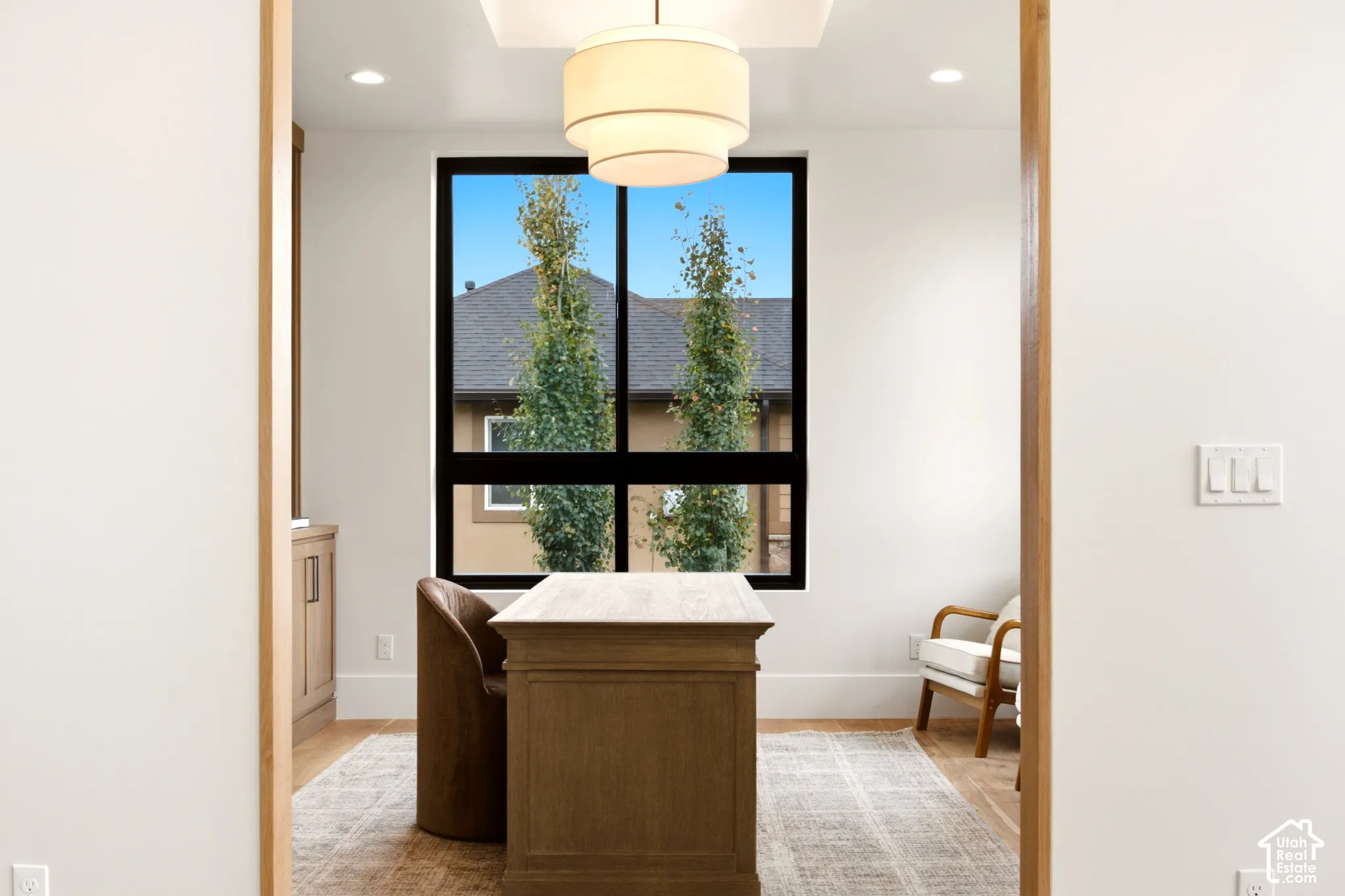 Rift sawn white oak framed doorway, large black frame window with tiered modern pendant light, reverse tray ceiling lighting, and built-in walnut cabinetry featuring metallic hardware