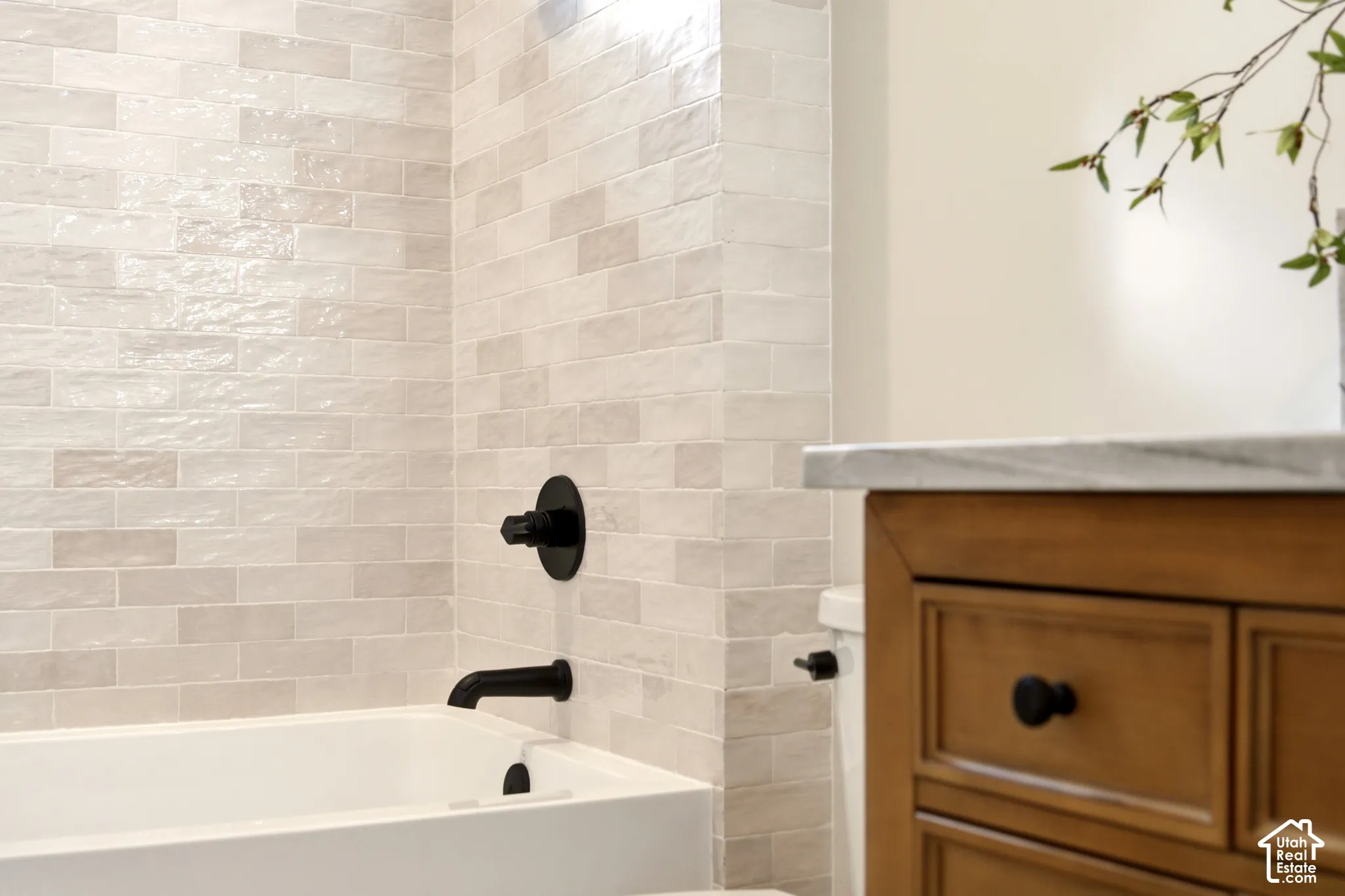 Textured Tile bar tile alcove tub surround, matte black wall-mounted fixtures, and wood stained vanity cabinet with a Denali Quartzite countertop