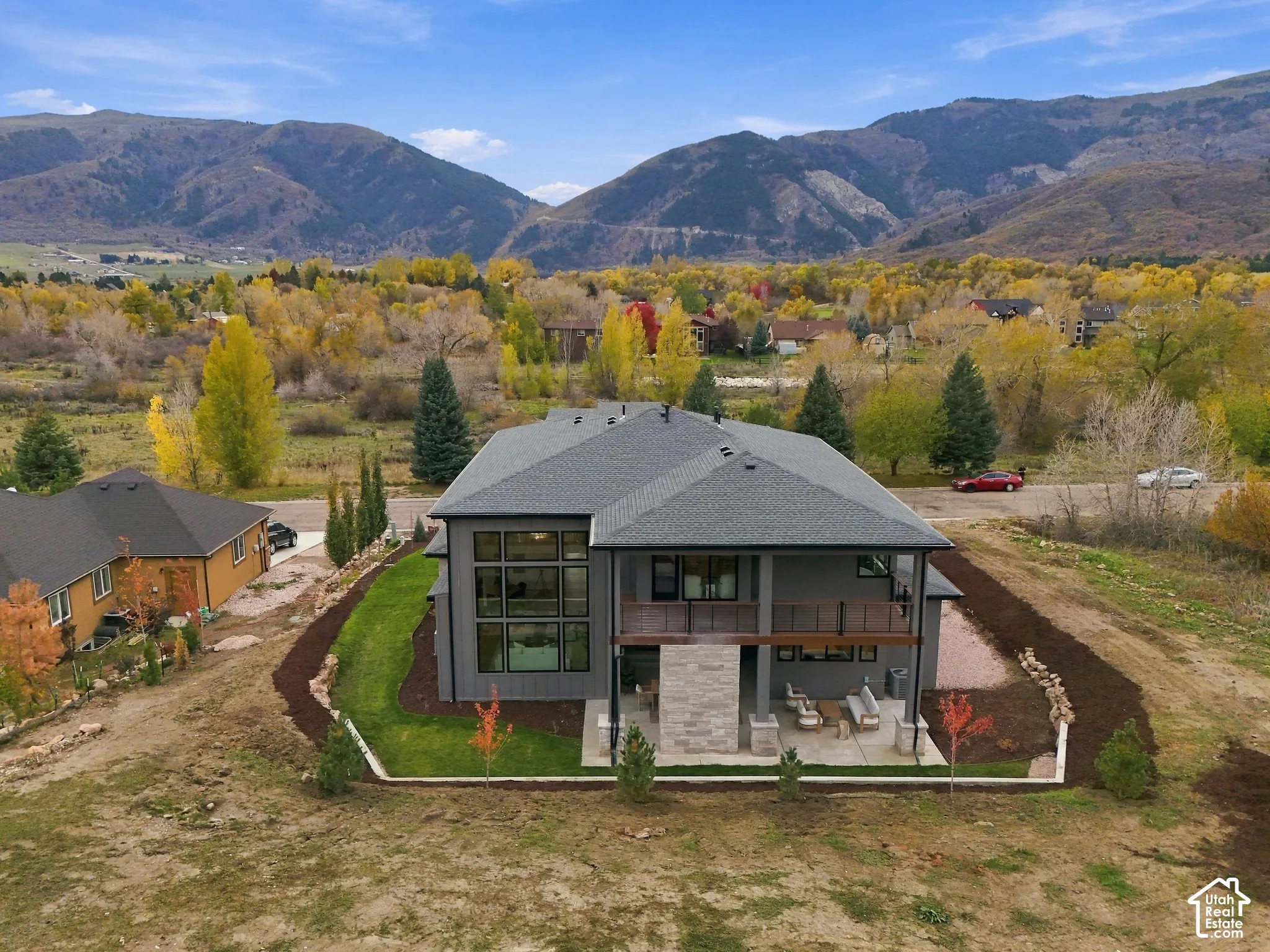 Multi-level exterior with expansive windows, natural limestone fireplace, covered patio, private primary balcony with horizontal rail system, and mountain backdrop