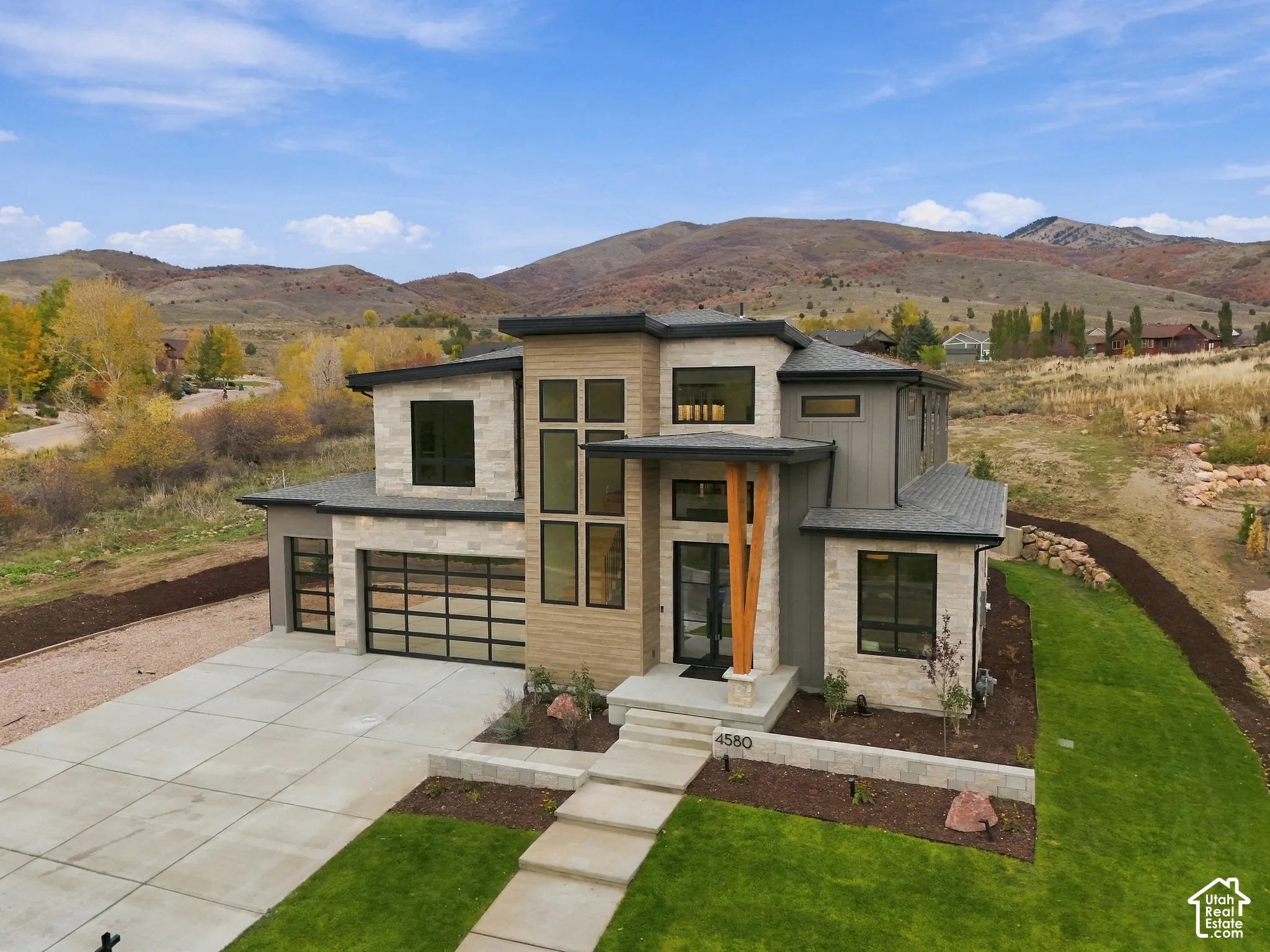 Contemporary exterior featuring dry-stacked natural limestone facade, Cham Clad Wood-look siding, multi-story glass paneling, double full view glass-paneled garage doors, set against a prominent mountain backdrop
