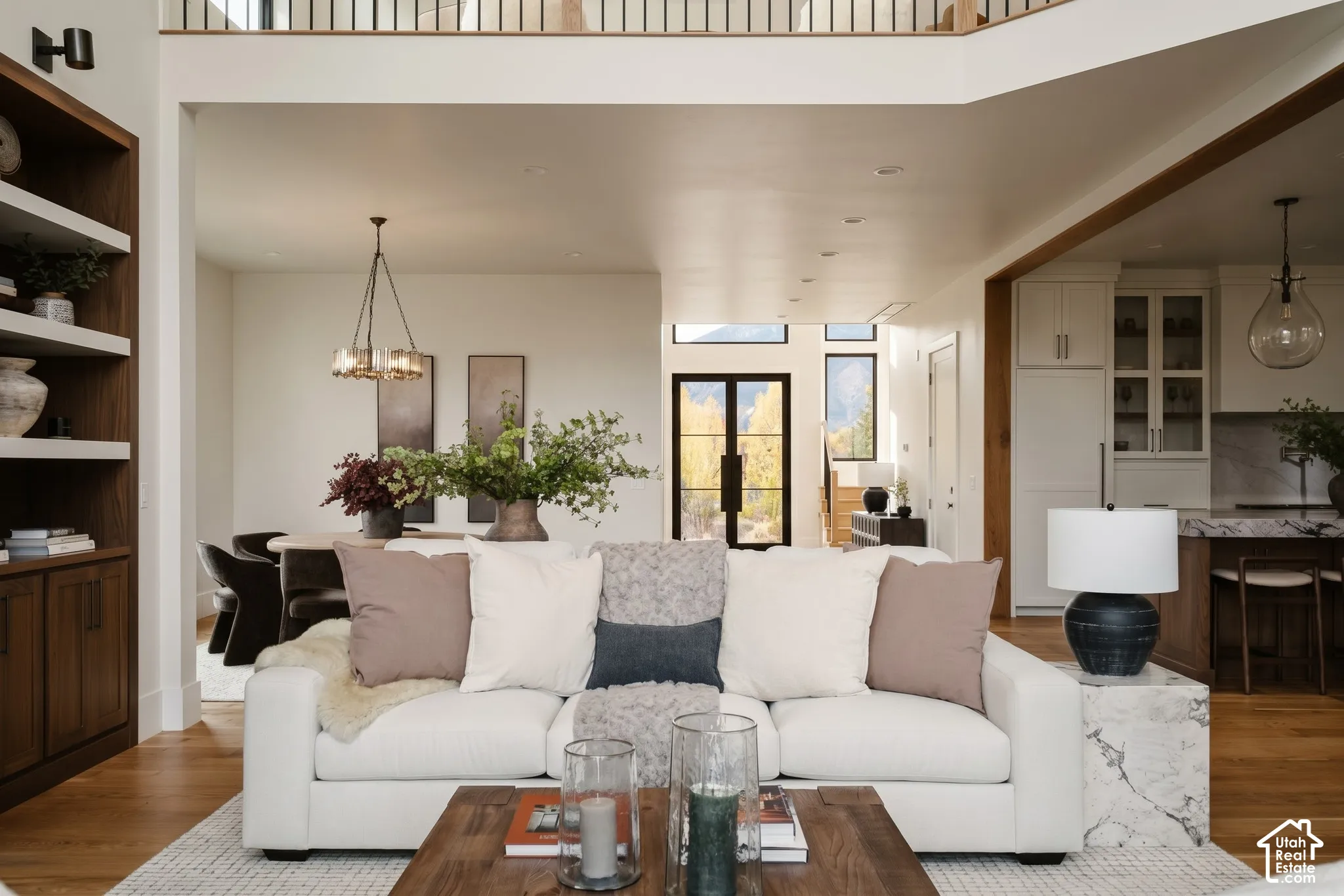 View through the 2-story great room capturing the natural light moving through the home. White oak accents, and kitchen visible