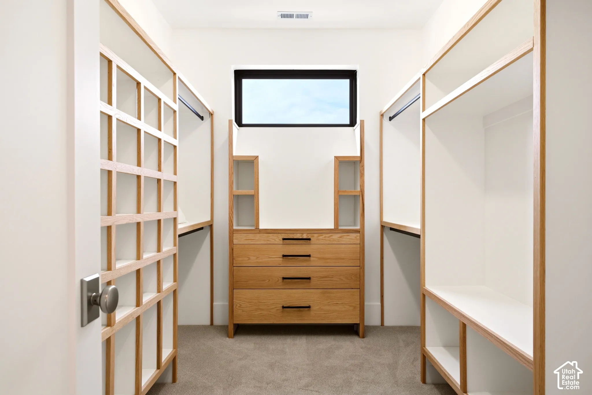 "Her" Walk-in Primary closet featuring custom oak-trim shelving, built-in dresser with Ash grey hardware, clerestory window, and carpeted flooring. (Not shown is the separate "His" Walk in closet)