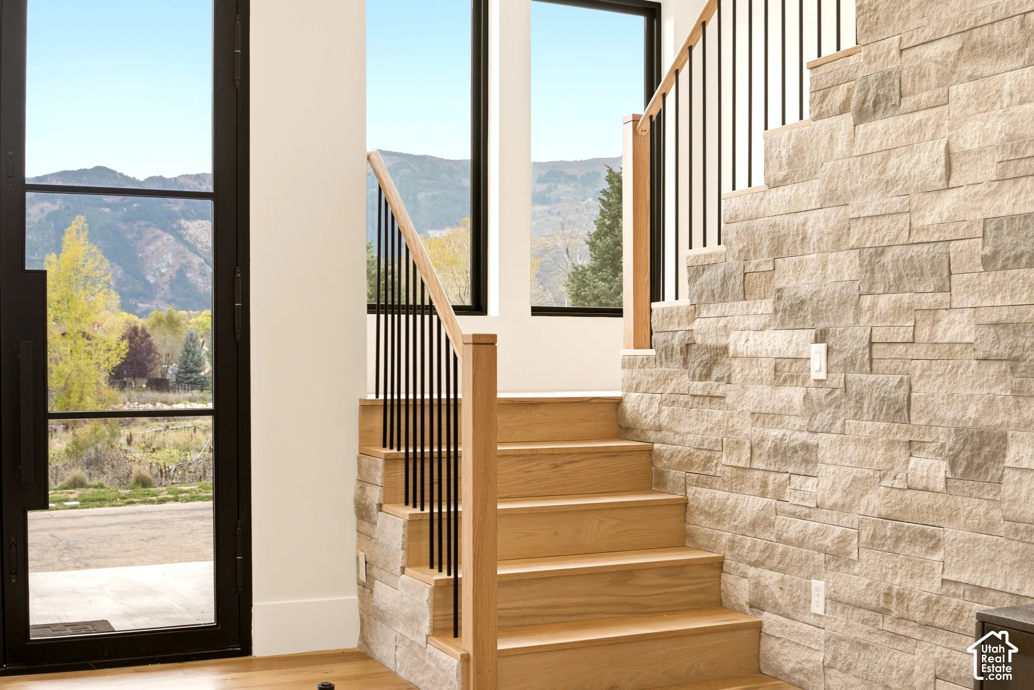 Staircase featuring Oak wood treads, dry-stacked limestone accent wall, railing, complemented by a 9' iron French door and mountain scenery