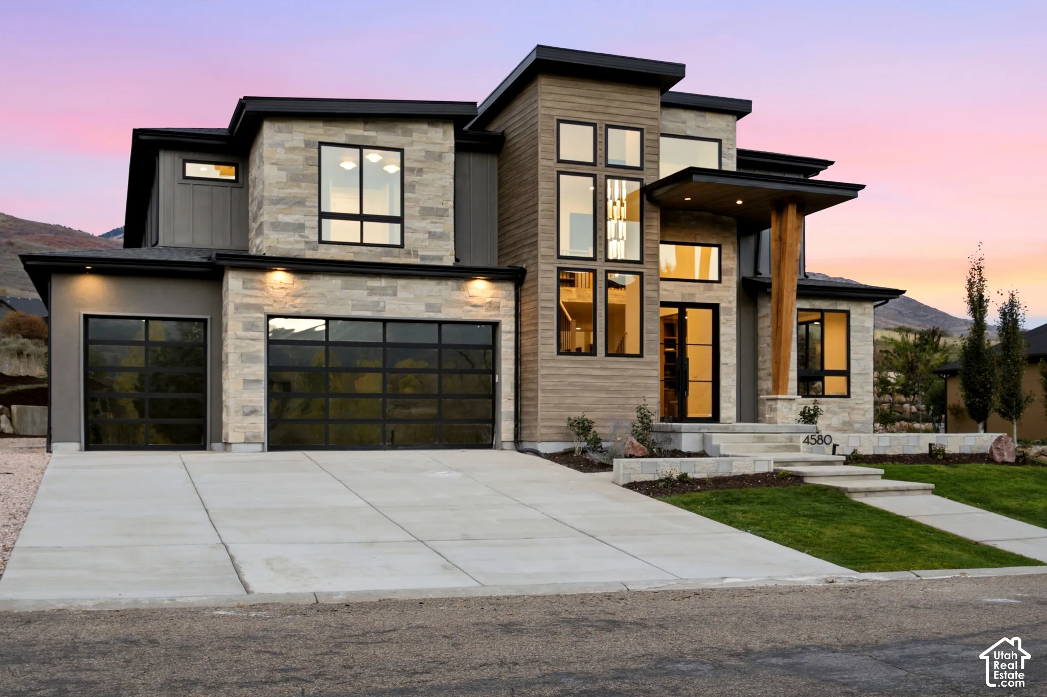 Modern exterior featuring natural limestone siding, horizontal wood-finish siding, full view tinted glass garage doors, multi-pane glass entryway, and a statement timber support