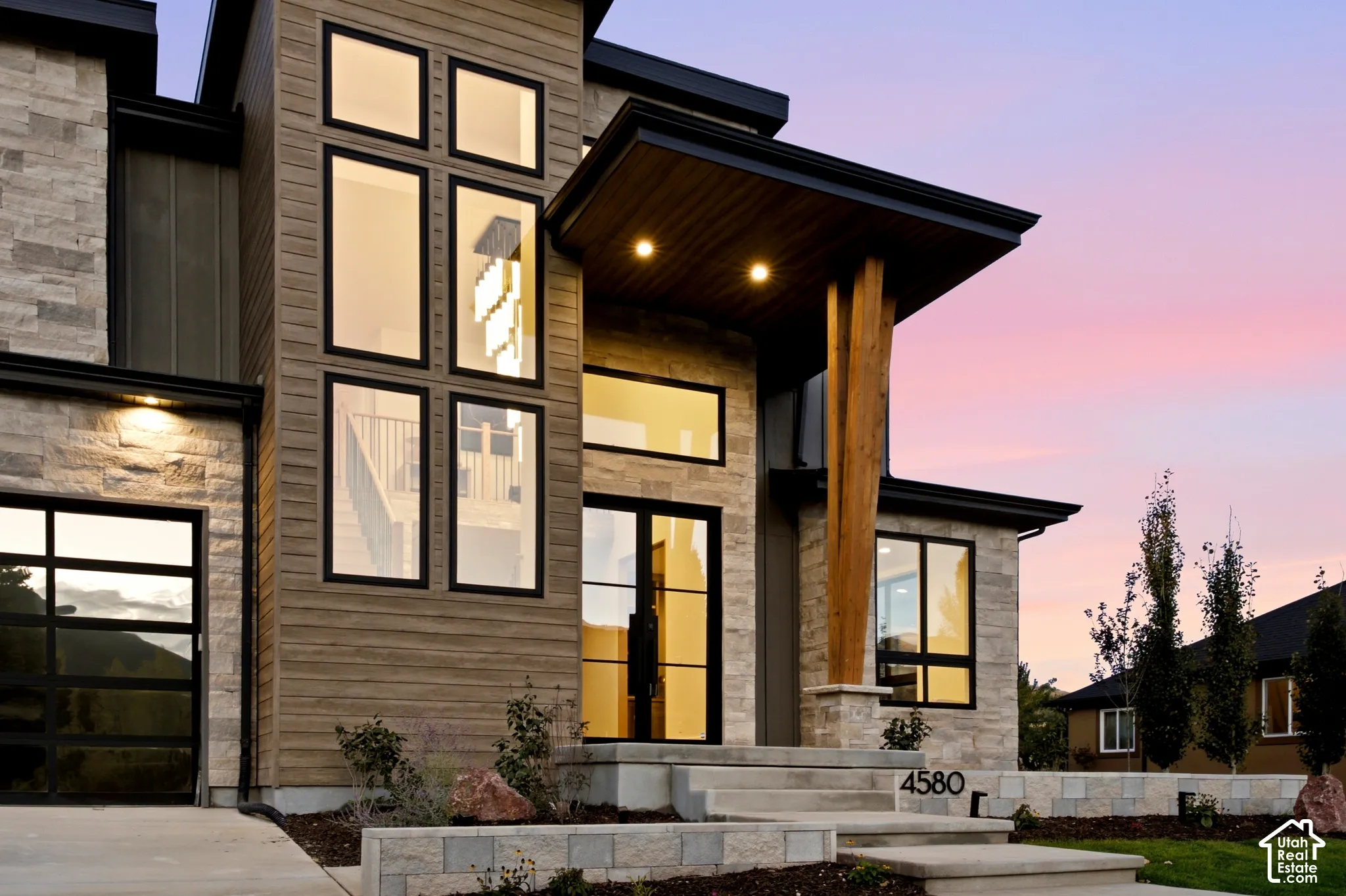 Modern exterior featuring natural limestone siding, horizontal wood-finish siding, full view tinted glass garage doors, multi-pane glass entryway, and a statement timber support