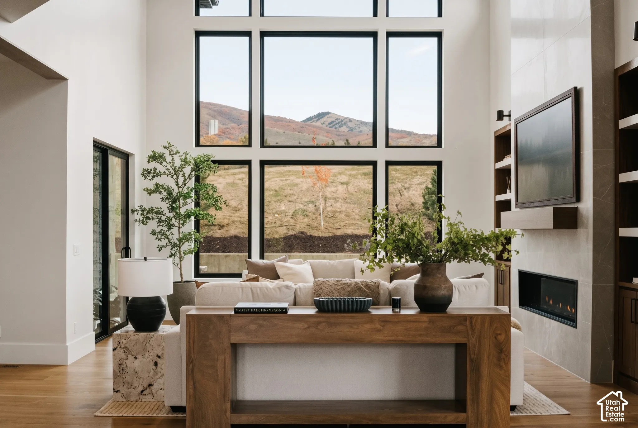20' Double-height ceiling, floor-to-ceiling windows with mountain scenery, engineered hardwood flooring, "Montego" 63" linear gas fireplace, with floor-to-ceiling tile surround, and built-in walnut cabinetry