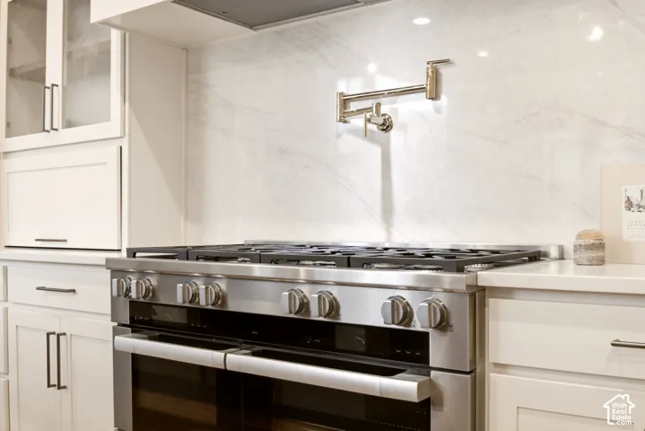 Miele 48" dual fuel double-oven range, Ivory Taj quartz backsplash, wall-mounted Kohler French Gold pot filler, custom appliance garage cabinetry with "Kokomo Seedy" glass-panel upper doors, and Ivory Taj Quartz countertop