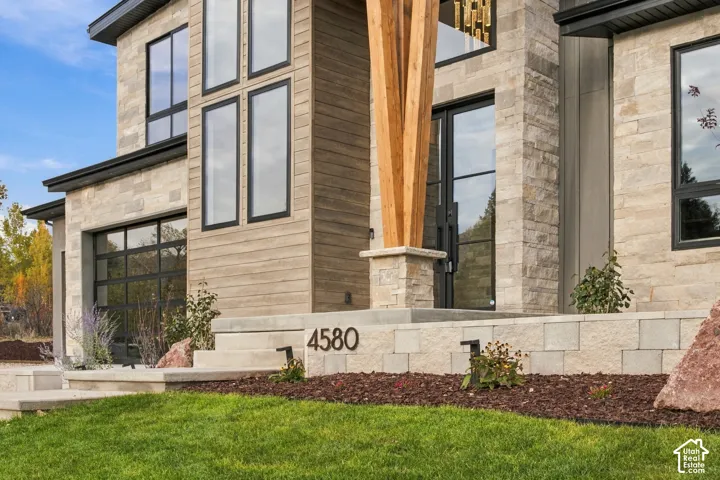 Modern exterior featuring natural limestone siding, horizontal wood-finish siding, full view tinted glass garage doors, multi-pane glass entryway, and a statement timber support