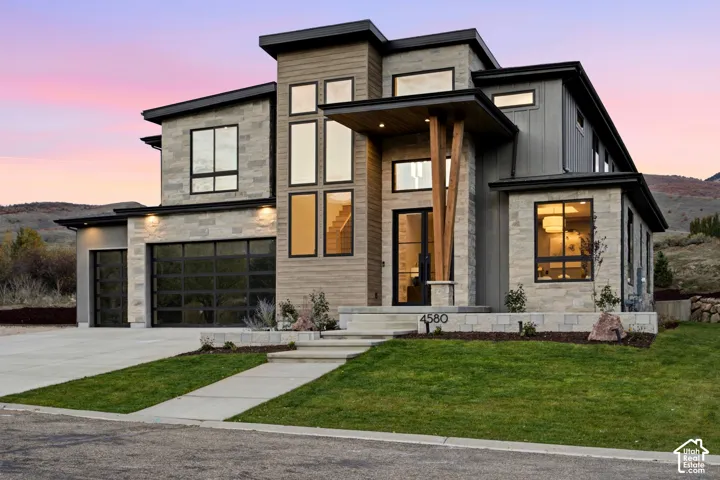 Modern exterior featuring natural limestone siding, horizontal wood-finish siding, full view tinted glass garage doors, multi-pane glass entryway, and a statement timber support