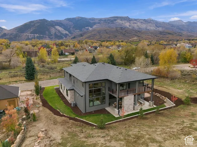 Multi-level exterior with expansive windows, natural limestone fireplace, covered patio, private primary balcony with horizontal rail system, and mountain backdrop