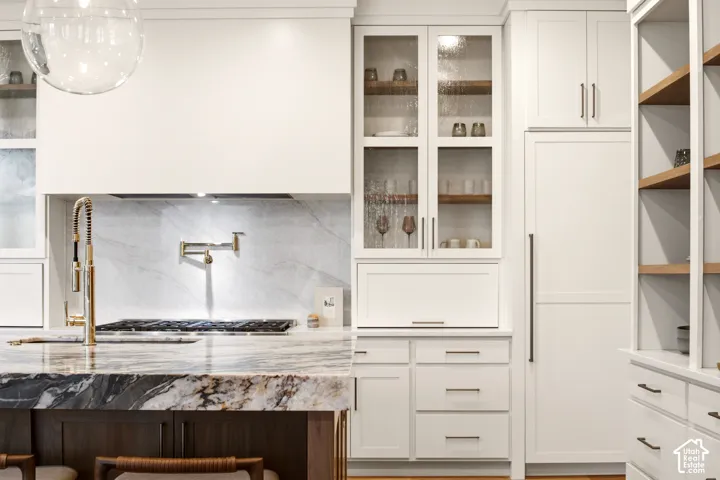 Kitchen featuring creamy white cabinetry with "kokomo seedy" glass-front uppers, "honed" Tempest Crystal-Quartzite center island, integrated Sub-Zero paneled refrigerator, Kohler French gold pot filler and faucet, and built-in walnut wood shelving